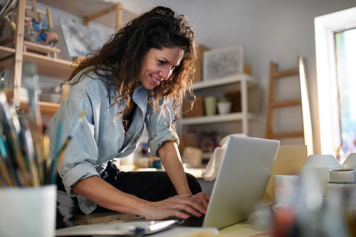 Happy young woman with laptop handles orders in pottery workshop - Representative Image Source: Getty Images | Photo by Halfpoint Images
