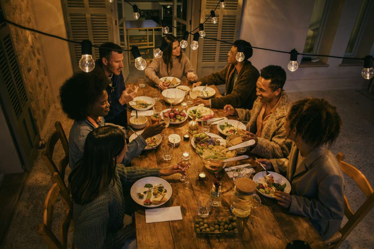 High angle view of smiling friends sitting at illuminated dining table during dinner party. (Representative Image Source: Getty Images | Photo by Mascot)