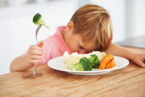 A cute young boy with his head on the table while holding a piece of broccoli on his fork. (Getty Images / People Images )
