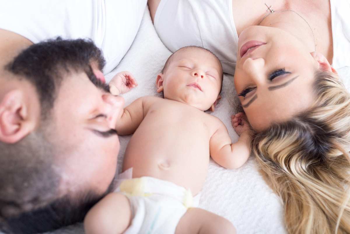 A baby sleeping between parents on the bed. (Image Source: Pixabay | smpratt90)
